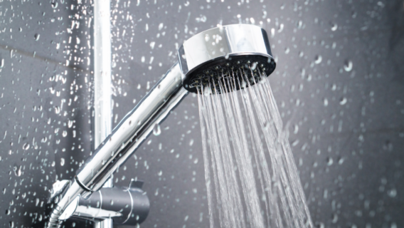 Chrome handheld showerhead spraying water against a dark, water-splashed tiled wall.