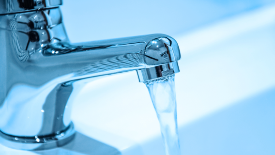 Close-up of a modern chrome bathroom tap with clear running water, representing water efficiency in new homes.