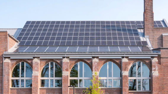 A large solar panel array installed on the roof of a brick commercial building with arched windows, showcasing a successful decarbonisation retrofit project.