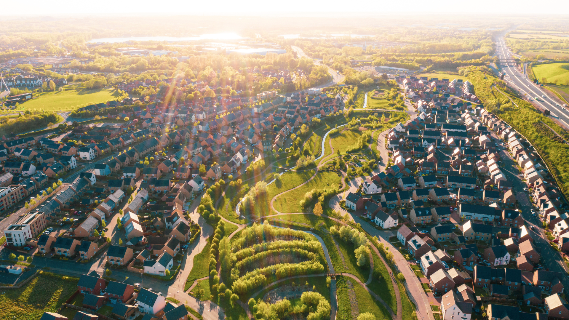 Aerial drone view of a large modern UK housing estate development at sunset, showcasing large-scale housing portfolios requiring Future Homes Standard modelling.