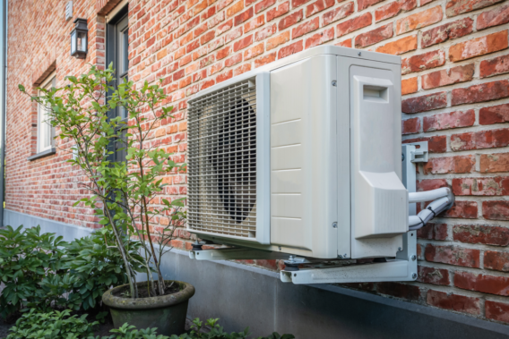 Air-to-air heat pump unit mounted on a brick house exterior, used to provide mechanical cooling.