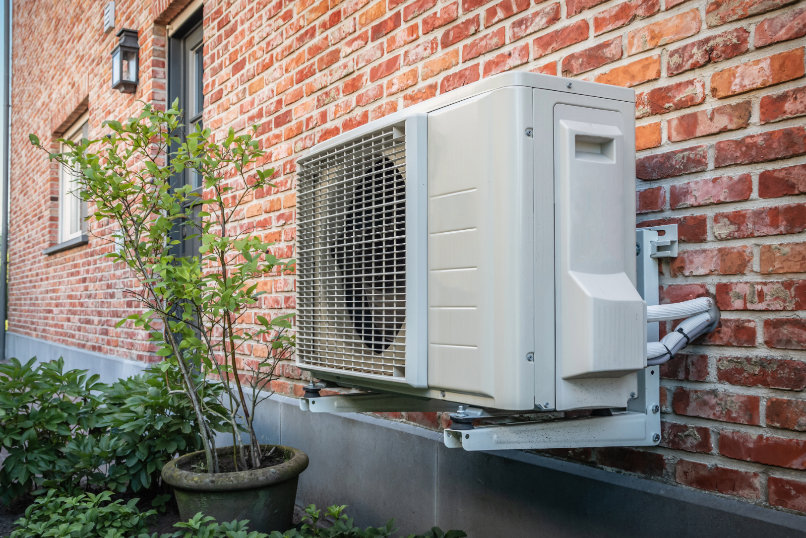 Air-to-air heat pump unit mounted on a brick house exterior, used to provide mechanical cooling.