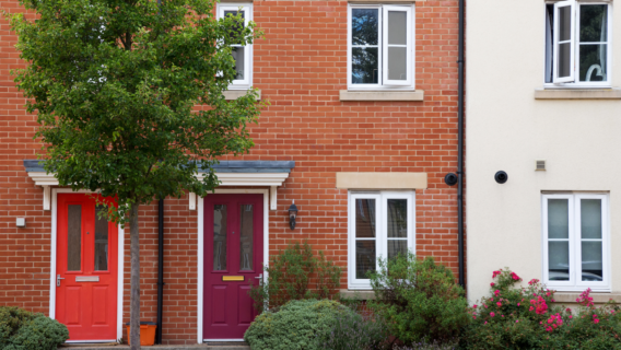 Modern brick terraced houses with red and maroon front doors, double-glazed windows and a front garden with shrubs and flowers