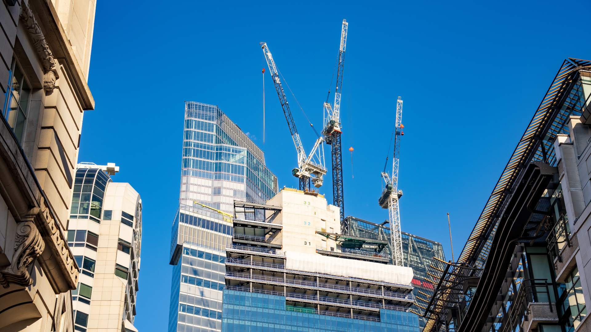 A high-rise commercial building under construction in the City of London, with its concrete core topped out and cranes still in use, surrounded by completed glass office towers.