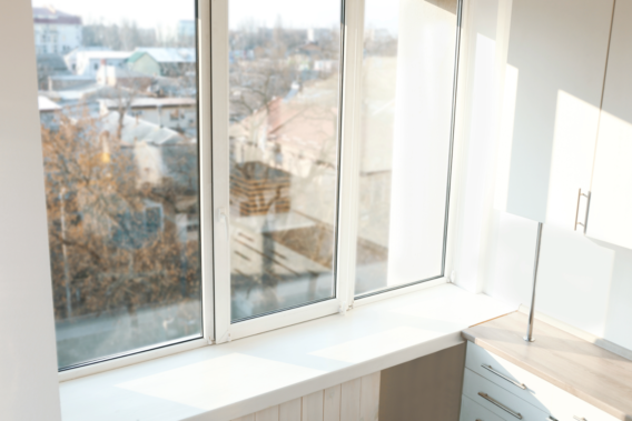 Large uPVC glazed window unit in a modern flat interior, with a wide windowsill, kitchen cabinetry, and a view over rooftops and trees outside.