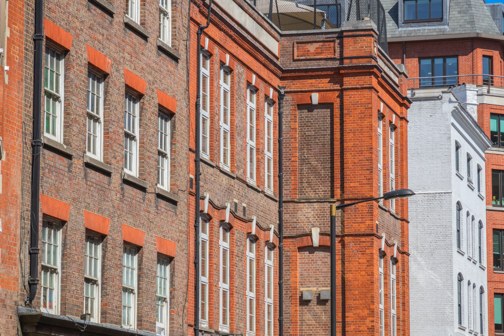 Row of red-brick period townhouses on a UK city street, with white sash windows and decorative stone detailing.
