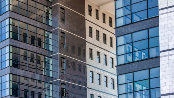 Close-up of a multi-storey commercial building facade, showing a mix of glazed curtain walling and tiled cladding panels in dark grey, charcoal and cream.