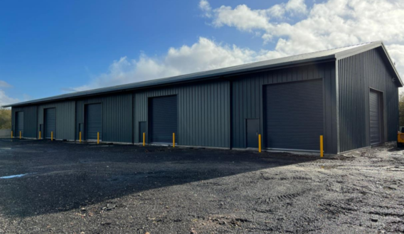 The newly completed industrial unit at Winkleigh Airfield, Devon, with grey metal cladding and five roller shutter doors on a gravel yard.