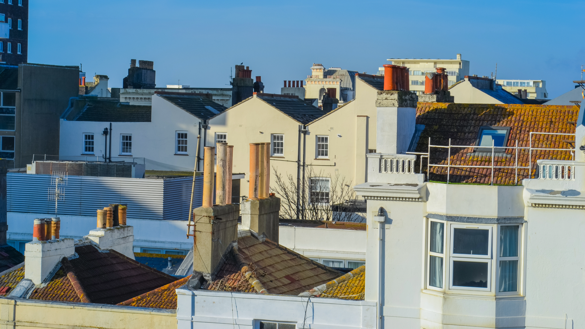 Rooftops of a dense Victorian terrace in Brighton, with rows of brick chimney stacks against a clear blue sky.
