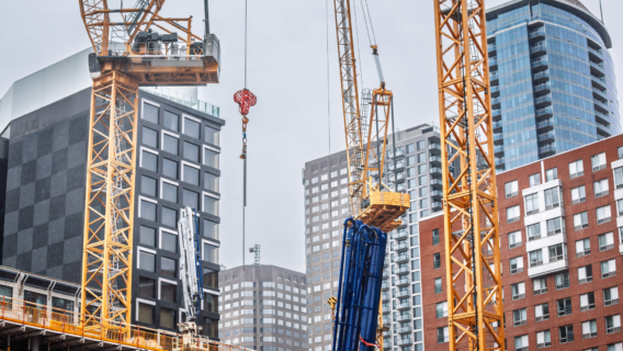 Tower cranes operating among modern high-rise commercial buildings under construction in a city centre.