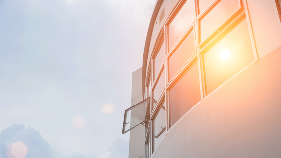 A commercial building facade with glass windows, one open, in strong sunlight with visible lens flare.