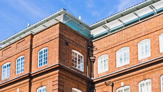 Close-up of a red brick building's upper corner, with white-framed arched windows and a modern glass-and-metal roof extension above.